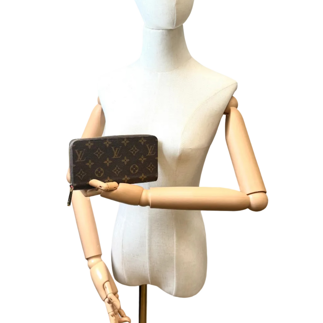 A Louis Vuitton monogram wallet or clutch held by a wooden-arm mannequin on a white background.