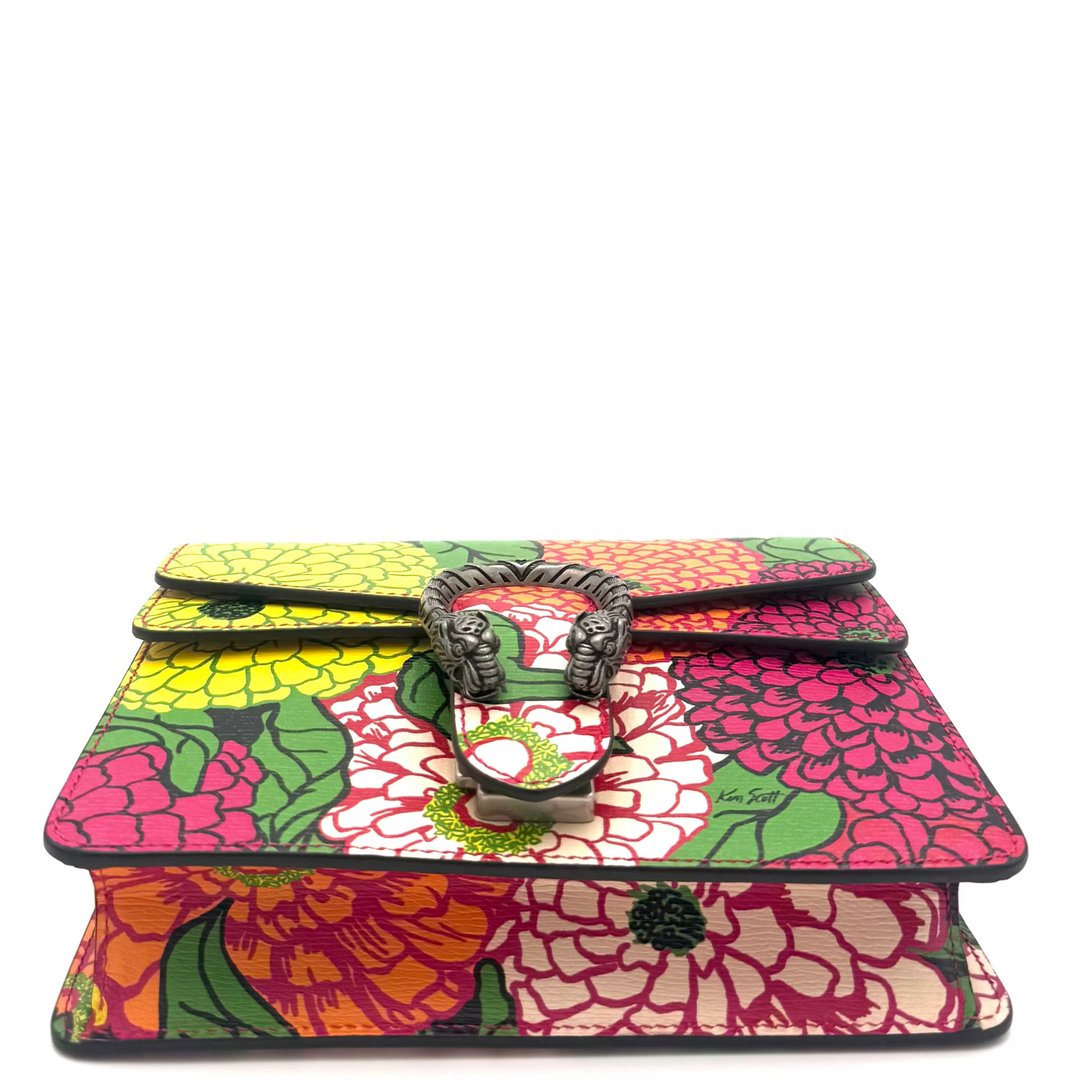 A small handbag with a vibrant multicolor floral print featuring pink, red, yellow, and green flowers, accented by a central metal lion head clasp.