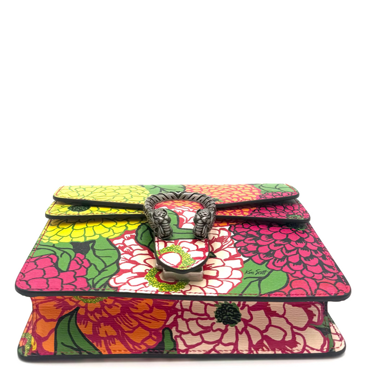 A small handbag with a vibrant multicolor floral print featuring pink, red, yellow, and green flowers, accented by a central metal lion head clasp.