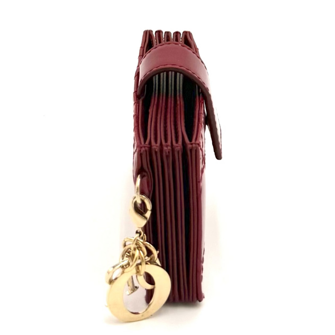 A small burgundy leather clutch with a gold-tone chain link charm, photographed on a plain white background.