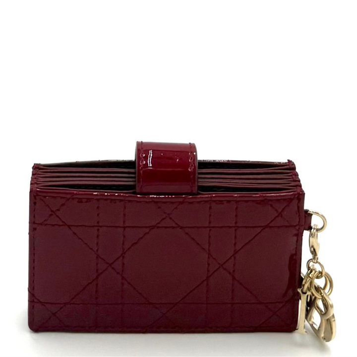 A burgundy patent leather clutch wallet with a quilted diamond pattern, a top handle, and a gold-tone chain keychain, shown on a white background.