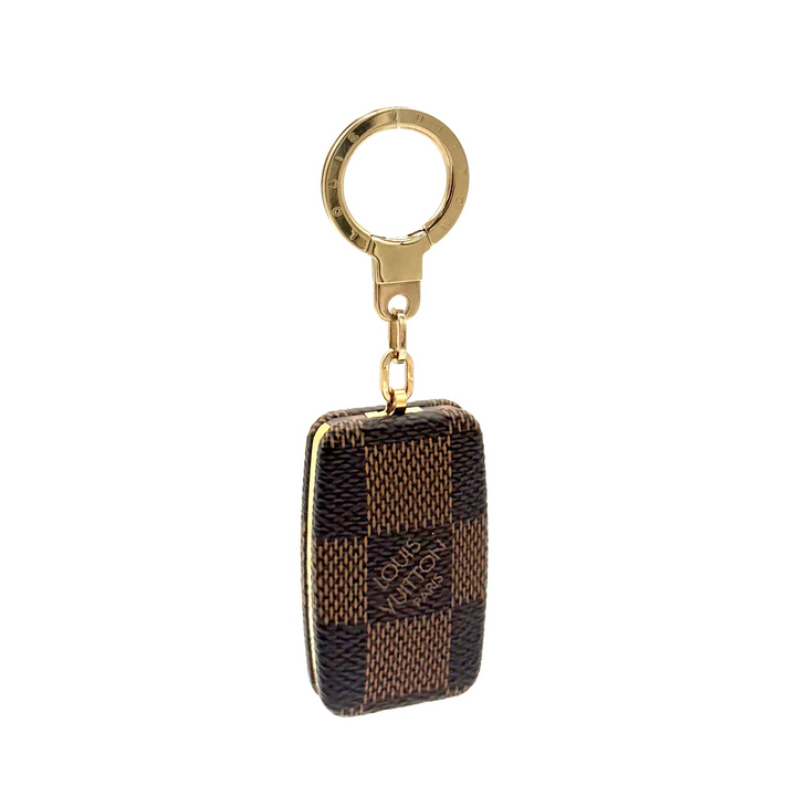 A Louis Vuitton Damier Ebene checkered keychain pouch with a gold-tone key ring, shown against a heavily overexposed white background.