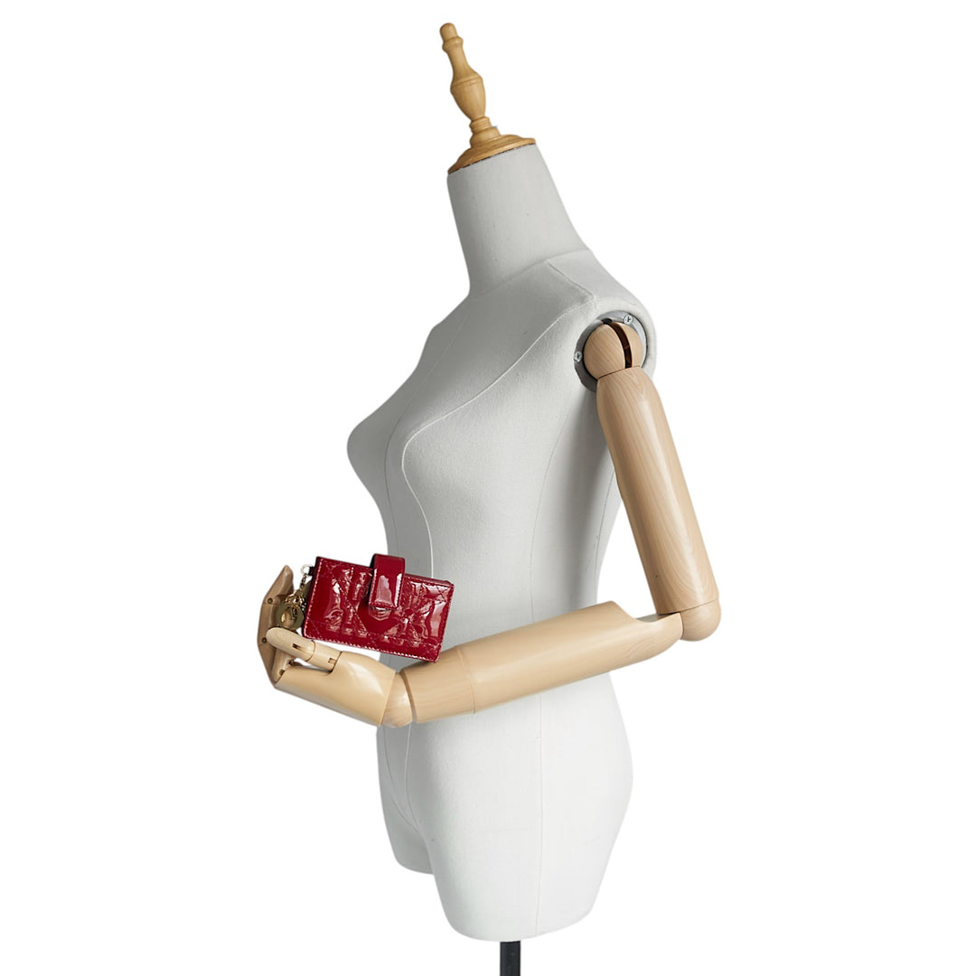 A small red textured clutch purse held by a white dress form mannequin with wooden arms against a plain white background.
