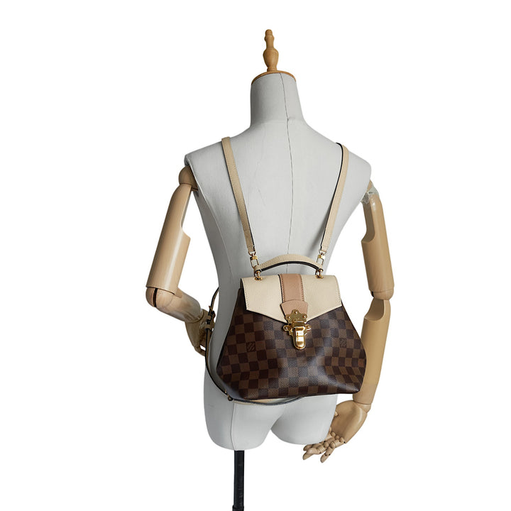A Louis Vuitton Damier Ebene canvas backpack with tan leather trim and gold-tone hardware, displayed on a beige mannequin torso against a white background.